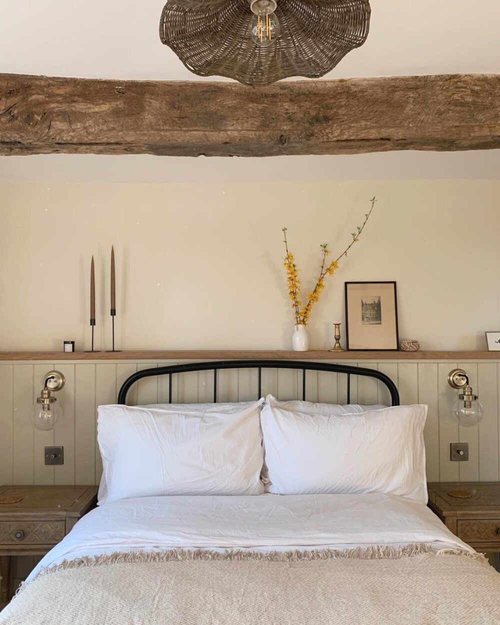 A black metal bed, styled in a rustic sage and white bedroom
